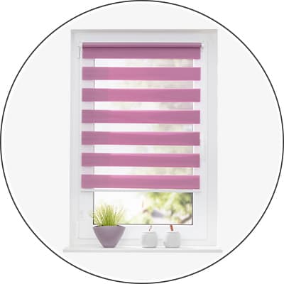 Rosa Doppelrollo am Fenster, davor Blumentopf mit Gras und zwei kleine Dekoobjekte auf der Fensterbank