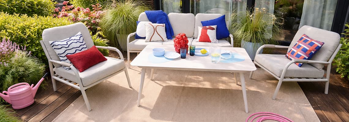 Gemütliche Gartensitzgruppe mit Sofa, Sesseln und bunt gemusterten Kissen rund um einen gedeckten Tisch auf der Terrasse