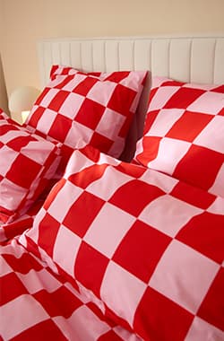 Bett mit Kopfteil, bezogen mit rot-rosa kariertem Bettbezug und passenden Kissen in Nahaufnahme