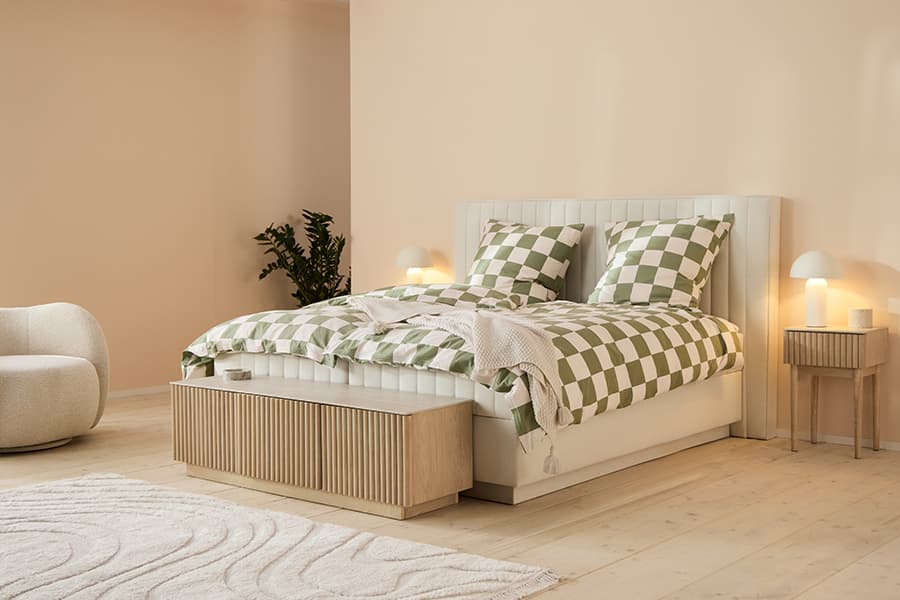 Doppelbett mit grün kariertem Bettbezug, zwei Kissen, Bank am Fußende, Nachttische mit Lampen in hellem Schlafzimmer