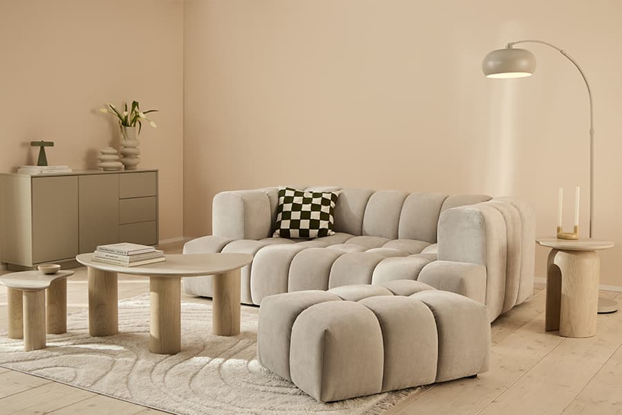 Beiges Wohnzimmer mit modularem Sofa und Hocker, kariertem Kissen, runden Holztischen, Sideboard und Stehlampe