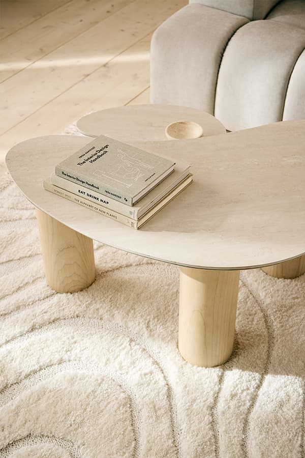 Organische Couchtischform mit drei Beinen, darauf gestapelte Bücher, daneben helles Sofa auf gemustertem Teppich