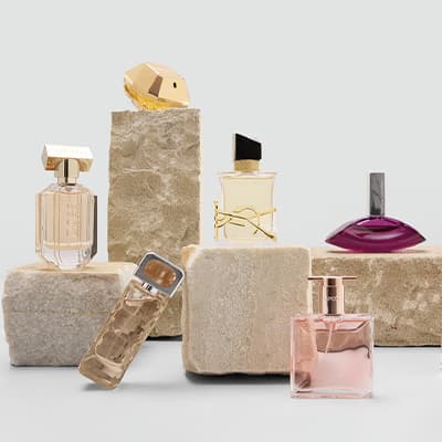 Mehrere Parfumflakons in verschiedenen Formen auf hellen Steinblöcken vor neutralem Hintergrund