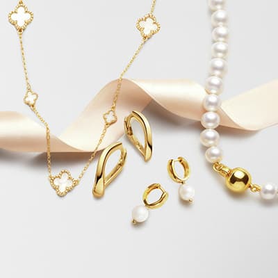 Goldfarbene Kette mit Blütenanhängern, goldene Ohrringe und Perlenkette auf hellem Untergrund mit Satinband