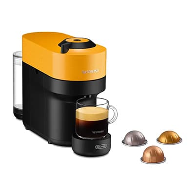 Nespresso-Kapselmaschine in Gelb mit Glasbecher voller Kaffee daneben drei bunte Kaffeekapseln auf weißem Hintergrund