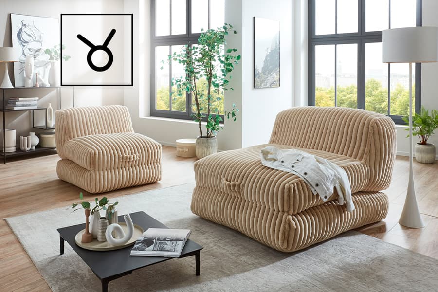 Wohnzimmer mit beigem Sessel und Sofa, davor Couchtisch, große Fenster mit Blick ins Grüne und Pflanzen im Raum