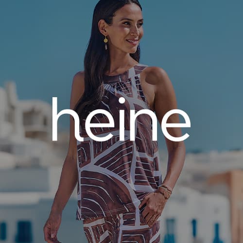 Frau im ärmellosen gemusterten Zweiteiler steht draußen vor hellen Häusern, Heine Logo mittig im Bild