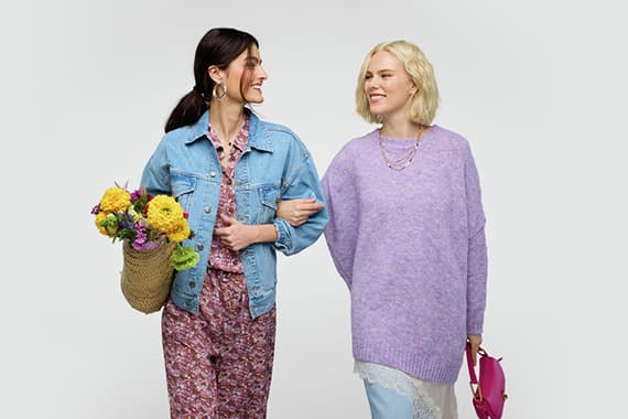 Zwei Personen stehen nebeneinander, eine hält einen Blumenstrauß, die andere trägt einen lila Pullover.