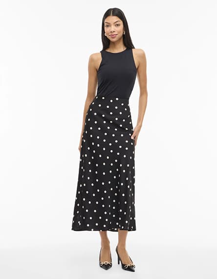 Frau trägt schwarzes ärmelloses Top und langen schwarzen Rock mit weißen Punkten, dazu schwarze Pumps
