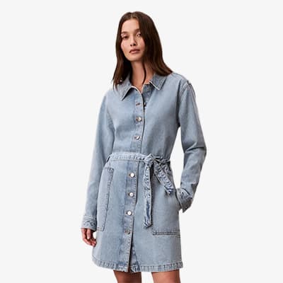 Frau trägt helles Hemdkleid mit Knopfleiste und Bindegürtel, steht leicht seitlich mit einer Hand in der Tasche