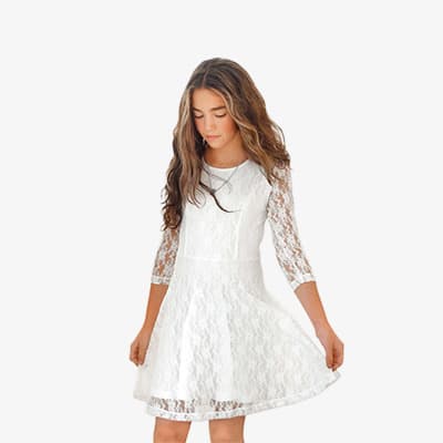 Mädchen mit langen Haaren in weißem Spitzenkleid hält den Rock mit beiden Händen leicht zur Seite