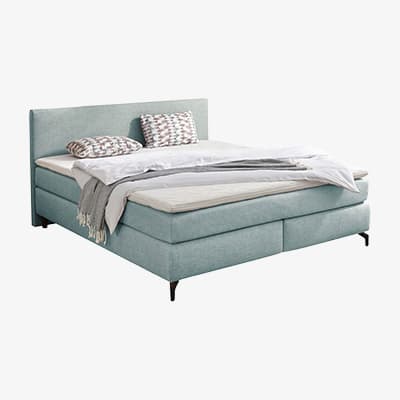 Doppelbett mit hohem Kopfteil, aufgeschlagener Decke und zwei gemusterten Kissen auf der Liegefläche