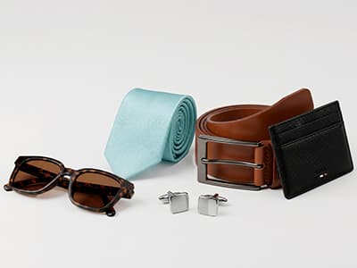Herrenaccessoires: hellblaue Krawatte, brauner Gürtel, schwarzes Kartenetui, Sonnenbrille und quadratische Manschettenknöpfe