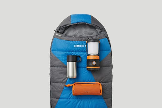 Schlafsack von oben mit Thermobecher, Campinglampe und tragbarem Lautsprecher ordentlich darauf angeordnet