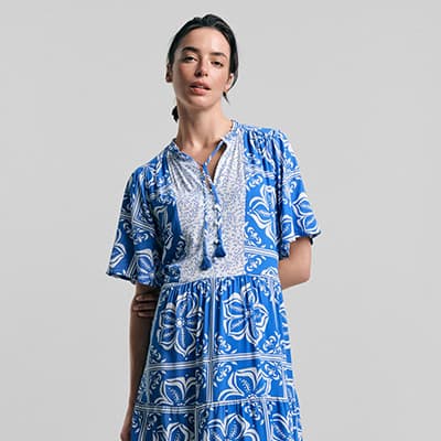 Frau mit schulterlangem Haar trägt knielanges blaues Kleid mit weißem Blumenmuster und kurzen Ärmeln