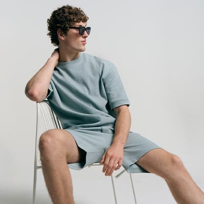 Mann in lockerem Shirt und Shorts sitzt lässig auf einem Stuhl und legt eine Hand in den Nacken