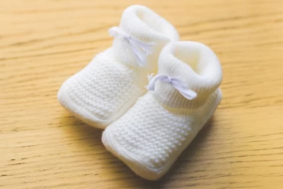 Weiße Baby-Socken mit kleinen Schleifen liegen nebeneinander auf einem Holztisch