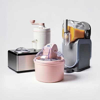 Vier Küchenmaschinen aufgereiht, rechts ein Entsafter mit frischem Orangensaft, vorne eine runde rosa Eismaschine