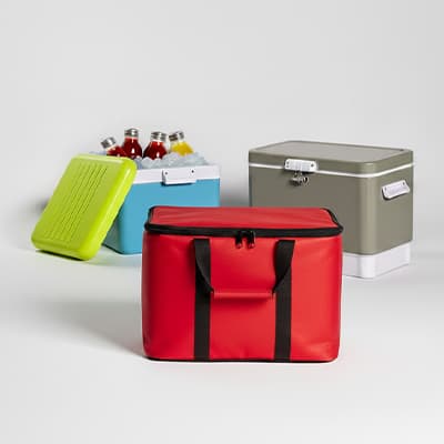 Rote Kühltasche im Vordergrund, dahinter offene blaue Kühlbox mit Getränken und graue Kühlbox mit geschlossenem Deckel