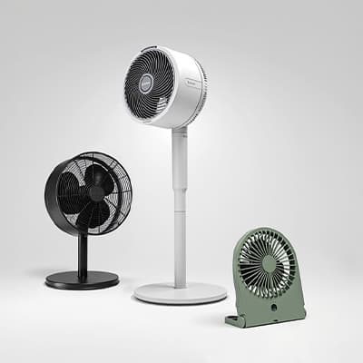 Drei unterschiedlich große Ventilatoren in Schwarz, Weiß und Grün stehen nebeneinander vor hellem Hintergrund