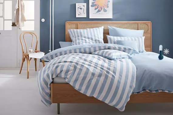 Doppelbett mit blau gestreifter Bettwäsche in hellblauem Schlafzimmer, Holzstuhl und Bilder an der Wand