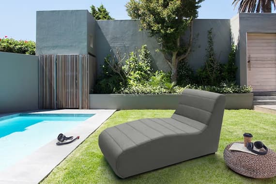 Graue Gartenliege auf Rasen neben Pool, im Hintergrund moderne Hauswand und Bäume