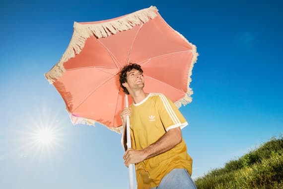 Person im gelben T-Shirt hält einen großen rosa Sonnenschirm auf einer Wiese unter blauem Himmel