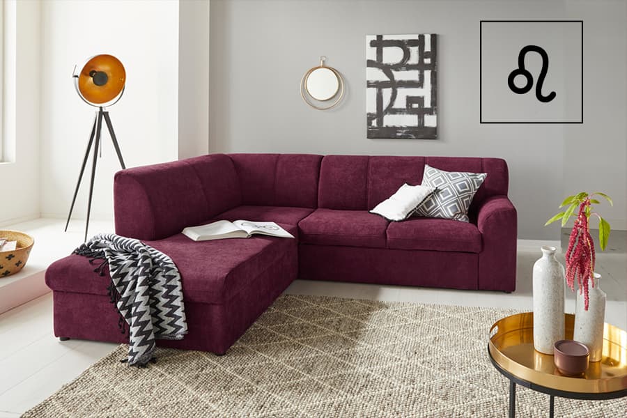 Ecksofa in L-Form mit Decke und offenem Buch, dekoriertem Couchtisch und Bildern an grauer Wand im Wohnzimmer