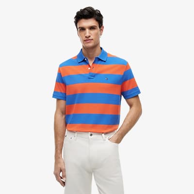 Mann im blau-orange gestreiften Poloshirt steht frontal zur Kamera und trägt eine helle Hose