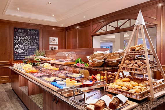 Großes Frühstücksbuffet mit Brotauswahl, Käse, Wurst, Obst und Cerealien auf Theke in holzvertäfeltem Raum