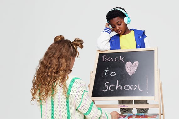 Back to school – Mädchen malt an einer Tafel, Junge mit Kopfhörern steht daneben und schaut zur Schrift