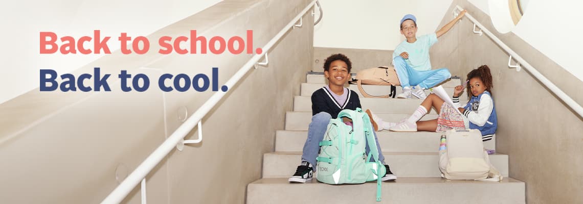 Back to school. Back to cool. – drei Kinder sitzen mit Rucksäcken auf einer Treppe und schauen zur Kamera