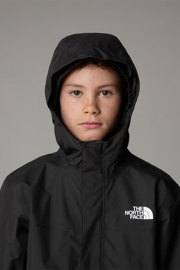 Kind mit hochgezogener Kapuze in schwarzer Jacke mit The-North-Face-Logo schaut frontal in die Kamera