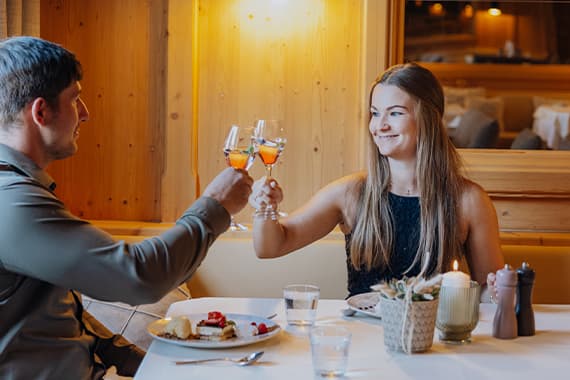Paar sitzt im Restaurant am Tisch und stößt mit gefüllten Sektgläsern über Tellern mit Dessert an