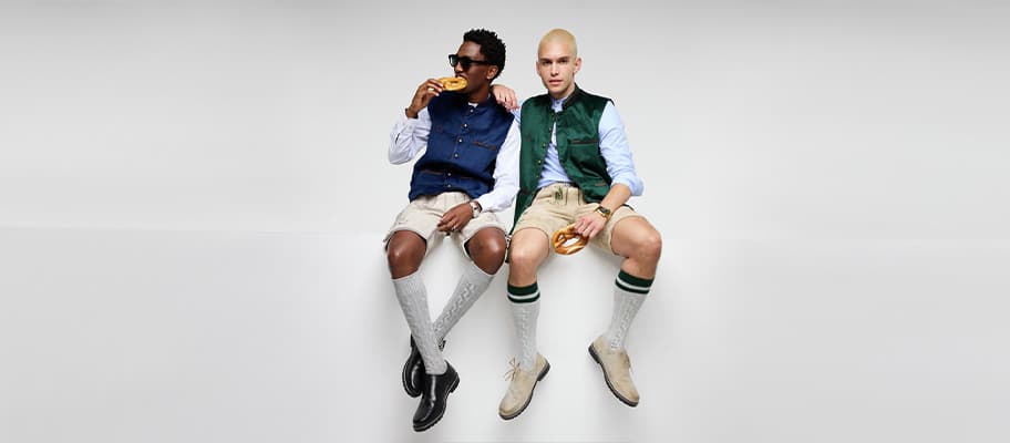 Zwei Männer in Trachtenlook sitzen nebeneinander und essen Brezeln, beide tragen Weste, kurze Hose und Kniestrümpfe