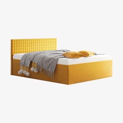 Doppelbett mit gelbem Kopfteil, grauer Decke mit Bommeln und zwei gelben Kissen auf weißer Matratze