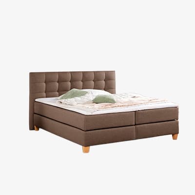 Doppelbett mit hohem, gestepptem Kopfteil, bezogener Matratze, Decke und zwei Kissen auf hellem Hintergrund