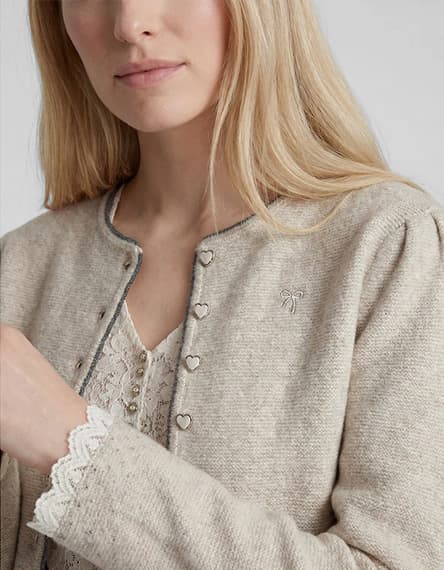 Frau mit offenem blonden Haar trägt beigefarbene Strickjacke mit Herzknöpfen und Spitzenoberteil darunter