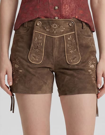 Frau trägt kurze braune Trachtenlederhose mit bestickter Latzklappe und seitlicher Blumenstickerei