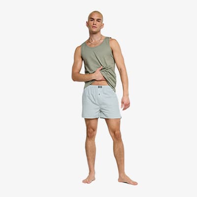 Mann im ärmellosen Oberteil und Boxershorts steht barfuß frontal und blickt in die Kamera