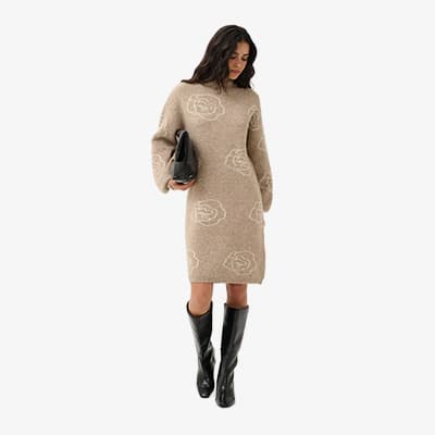 Frau im knielangen beigen Kleid mit Blumenmuster, hält schwarze Clutch und trägt hohe schwarze Stiefel