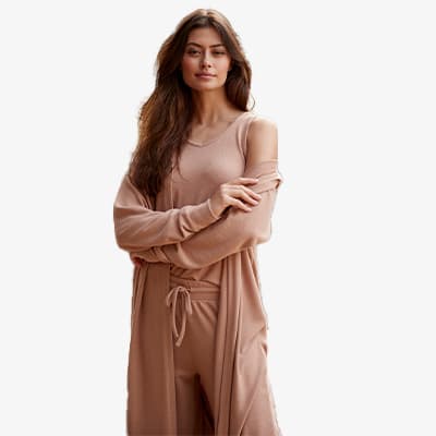 Frau mit langen Haaren trägt eine beige Loungewear-Kombination aus Oberteil, Hose und Mantel