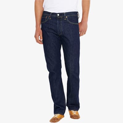 Mann trägt dunkelblaue Jeans und ein weißes T-Shirt, steht aufrecht, Hände locker an den Seiten, braune Schuhe an den Füßen.