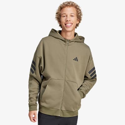 Mann in olivgrüner Kapuzenjacke mit schwarzen Streifen auf den Ärmeln und Logo auf der Brust, Hände in den Taschen.