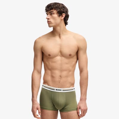 Mann in grünen Boxer-Shorts mit BOSS-Logo am Bund steht vor weißem Hintergrund, Gesicht unscharf