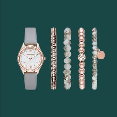 Graue Armbanduhr mit roségoldenen Details neben fünf verschieden gestalteten Armbändern in Roségold und Weiß