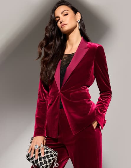 Frau mit langen Haaren trägt weinroten Anzug und hält silberne Clutch in der Hand