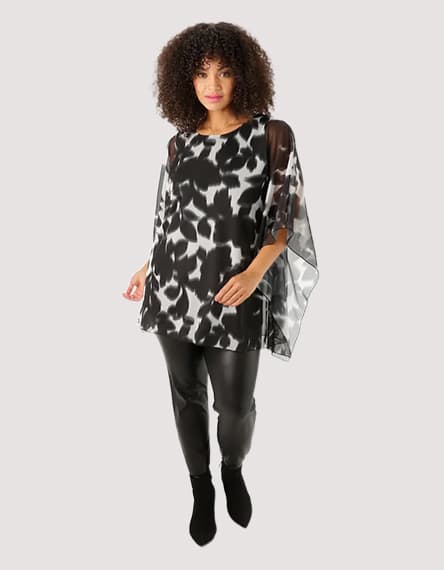 Frau in schwarz-weiß gemusterter Tunika und schwarzen Leggings posiert.