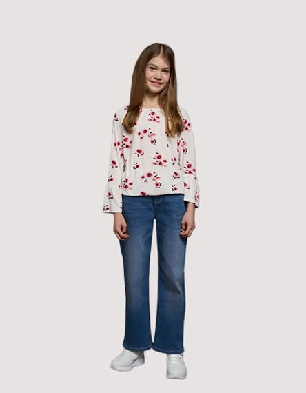 Mädchen trägt ein weißes Oberteil mit roten Blumen und blaue Jeans, weiße Schuhe