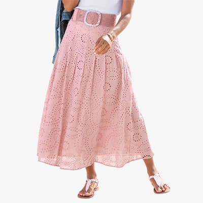 Frau trägt einen rosa langen Rock mit ausgestanztem Muster und Gürtel, dazu weiße Sandalen.